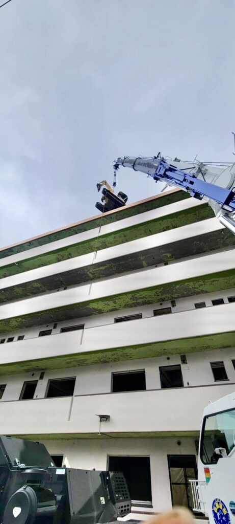  大型クレーンで建物上部へ重機を吊り上げて搬入する作業風景